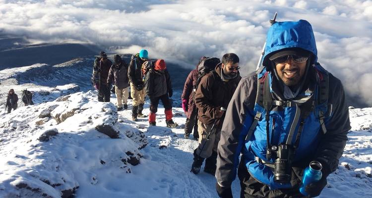 Groupe de randonneurs sur un sentier de montagne enneigé avec des nuages en contrebas.
