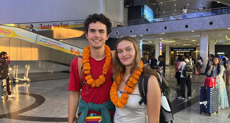 Jeune couple portant des guirlandes de souci posant joyeusement dans un terminal d'aéroport sous des lumières artificielles brillantes.