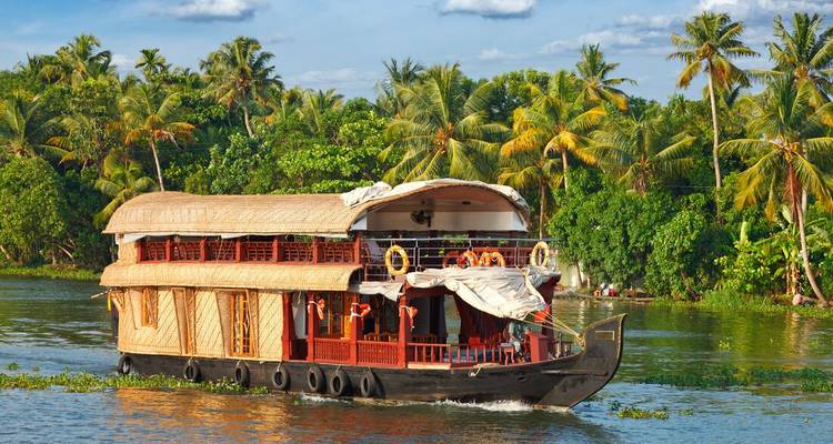 Bateau-maison traditionnel aux toits de chaume du Kerala glissant le long des backwaters luxuriants bordés de palmiers