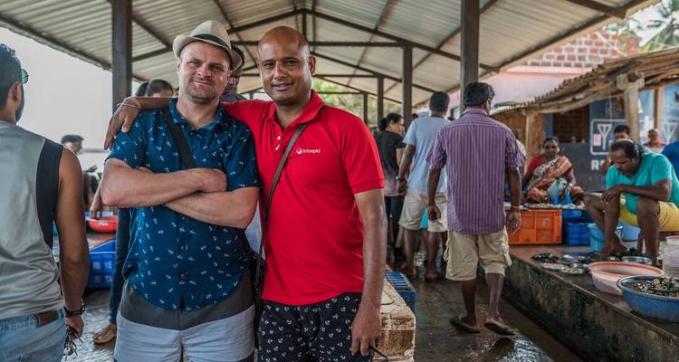 Deux voyageurs posent dans un marché aux poissons couvert animé avec des habitants en arrière-plan