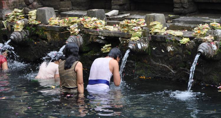 Des personnes effectuant un rituel aquatique sur un site sacré avec des sculptures en pierre et de l'eau courante