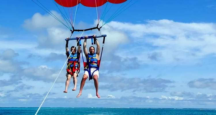 Deux personnes faisant du parachute ascensionnel au-dessus de l'océan avec un ciel bleu.