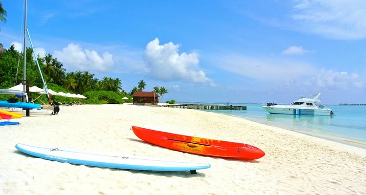 Plage ensoleillée avec des kayaks et un yacht au loin.