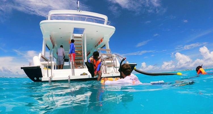 Des gens dans l'eau près d'un bateau avec un océan et un ciel d'un bleu éclatant.