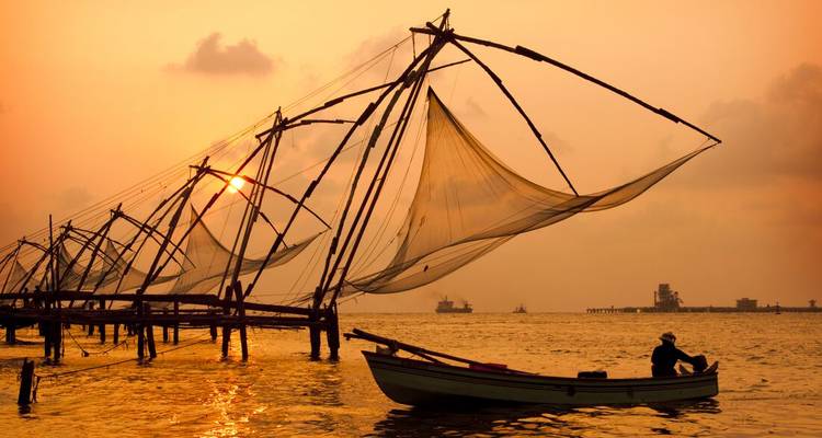 Les filets de pêche chinois en silhouette et une petite embarcation dans le port de Kochi au coucher du soleil.