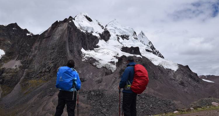 Dos excursionistas con mochilas disfrutando de un paisaje montañoso nevado.