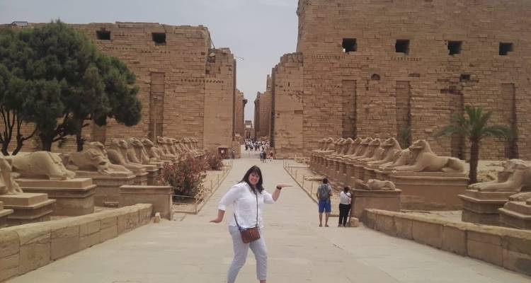 Personne posant devant des ruines de temple ancien avec des statues bordant le chemin.