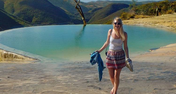 Voyageur se tenant pieds nus à côté d'une piscine à débordement turquoise surplombant les montagnes ondulantes