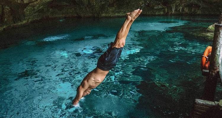 Un homme athlétique plonge tête première dans les eaux bleu clair d'un cénote mexicain à l'intérieur d'une caverne.