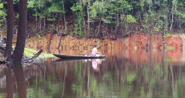 Une personne pagayant tranquillement en canoë sur une rivière calme entourée de forêt.
