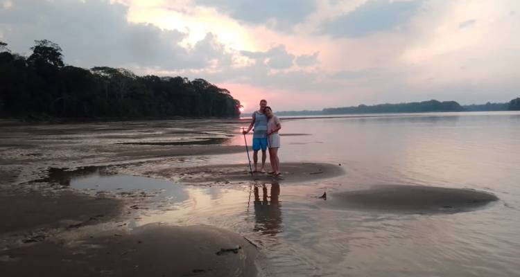 Una pareja parada en la orilla del río durante el atardecer.