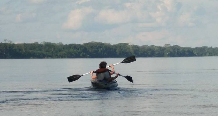 Persona navegando en kayak en un río ancho bajo cielos nublados.