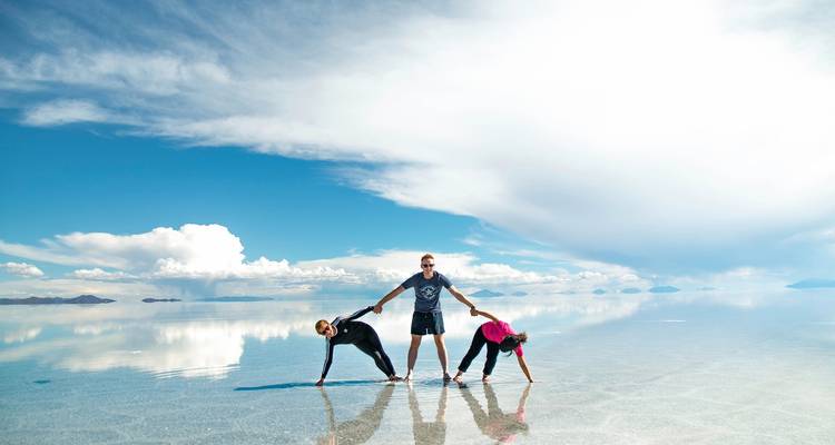 Three people posing on reflective salt flats with clouds above.