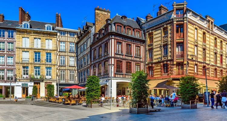 Des cafés en terrasse sur une place française entourée de bâtiments colorés.