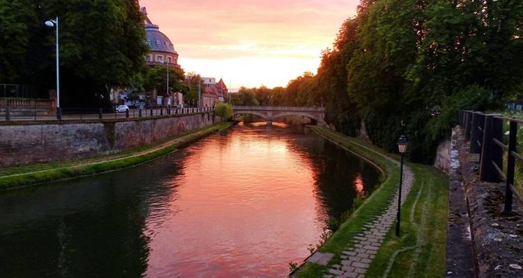Canal au coucher du soleil avec un pont et des bâtiments historiques.