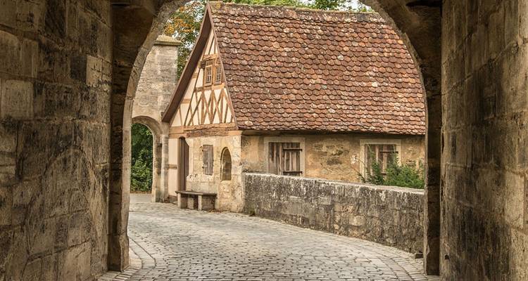 Vue à travers une arche sur une rue pavée et un bâtiment historique.