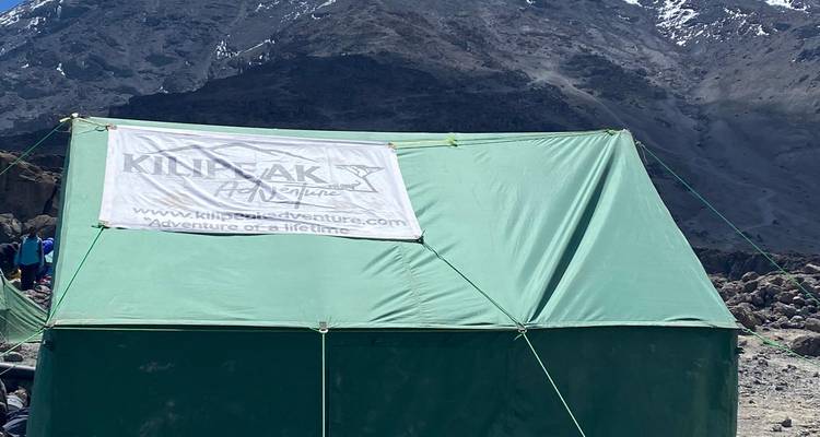 Grünes Zelt mit Kilipeak-Banner in einer bergigen Gegend.