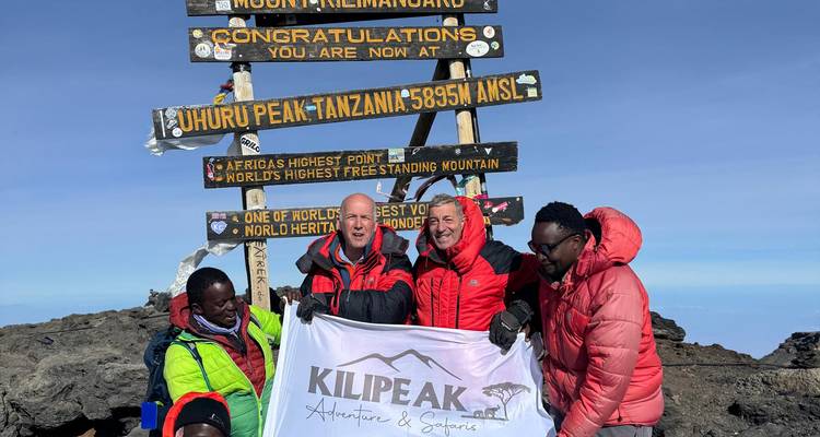 Bergsteiger feiern an dem Gipfelschild des Uhuru Peak auf dem Mount Kilimandscharo.