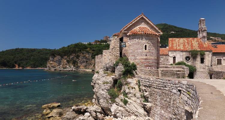 Historisches Küstengebäude mit Hügeln und blauem Meer.