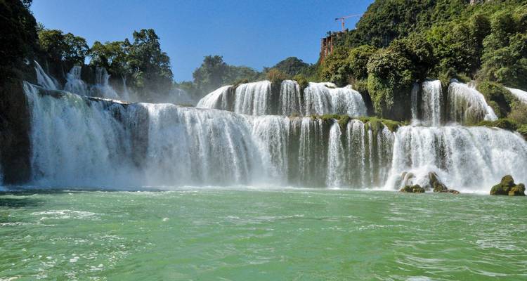 La puissante cascade de Ban Gioc à plusieurs niveaux se jette dans une eau turquoise sous un ciel bleu clair.