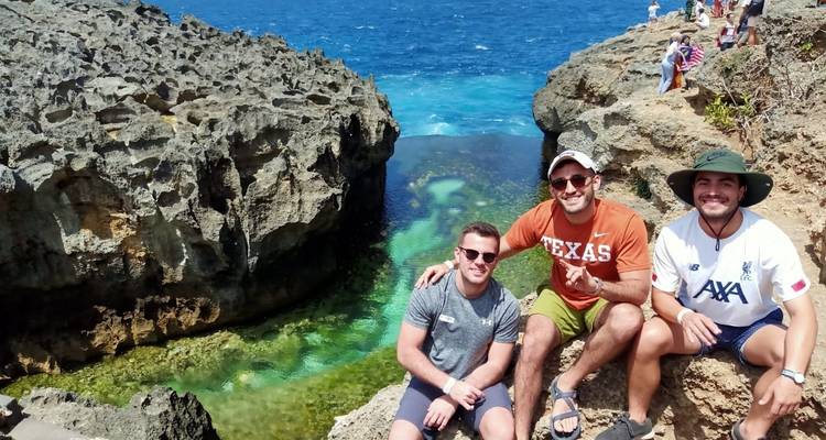 Trois hommes posant sur des falaises rocheuses avec un océan bleu clair.