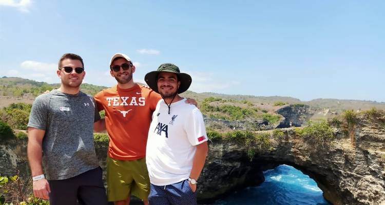 Trois hommes posant près d'une arche rocheuse naturelle au-dessus de la mer.