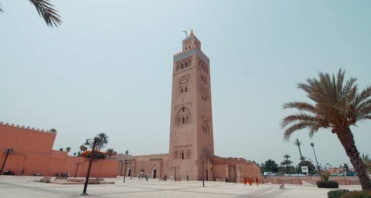 Hohes Minarett umgeben von einem offenen Platz mit Palmen.