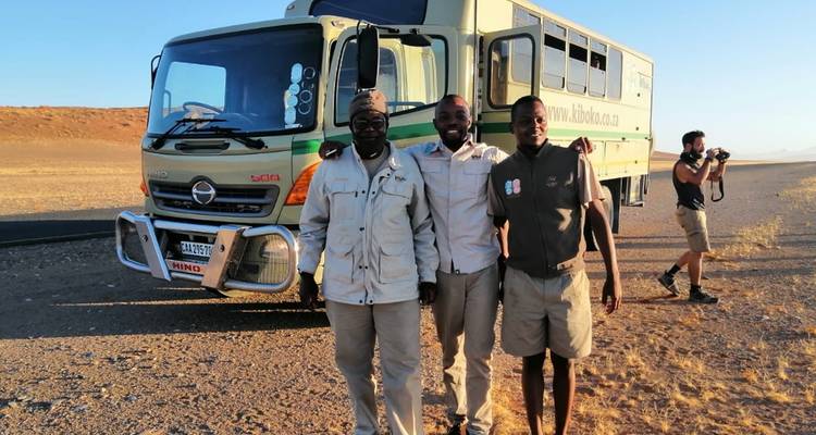 Tres hombres parados frente a un autobús turístico.