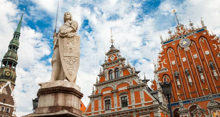 La estatua y los ornamentados gremios de la Casa de los Cabezas Negras de Riga se alzan contra un cielo azul nublado.