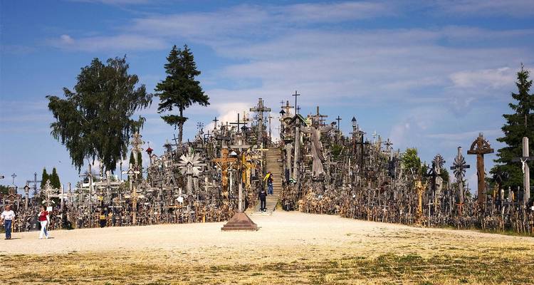 Feld mit Tausenden von hölzernen Kreuzen und Kruzifix-Figuren, die auf einem kleinen Hügel unter blauem Himmel gestapelt sind, Besucher, die zwischen ihnen gehen.