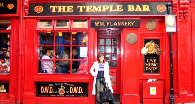 Façade rouge vif du célèbre pub Temple Bar de Dublin avec une femme posant à l'extérieur et des clients visibles à travers les fenêtres.