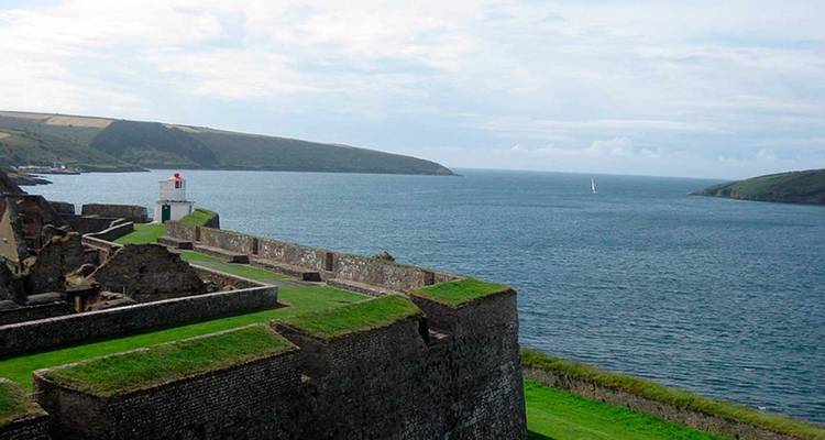 Les remparts en pierre d'un fort côtier s'étendant vers une mer bleue calme et des falaises verdoyantes ondulantes.
