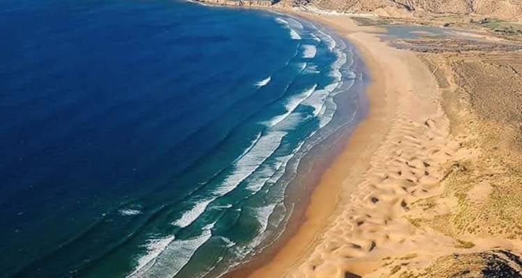 Wijd uitzicht op een afgelegen strand met zachte golven en een zandige kustlijn.