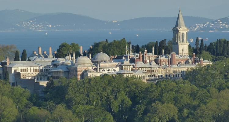 Elevated view of Topkapi Palace complex nestled amid trees with the Bosphorus and hills beyond.