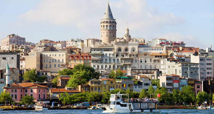 Galata Tower rises above a colorful waterfront district as boats cruise along the Bosphorus in Istanbul.