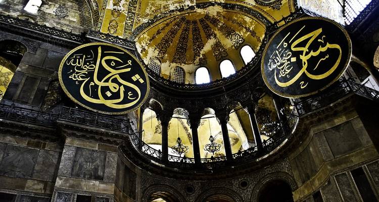 Richly decorated interior of Hagia Sophia with ornate calligraphy medallions and golden domed ceiling.