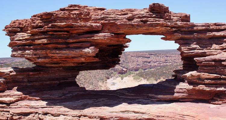 Arche rocheuse naturelle encadrant une gorge rouge escarpée et un lit de rivière lointain sous un ciel dégagé