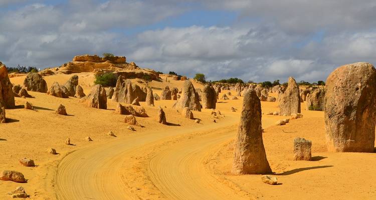 Des pics de calcaire sculptés par le vent s'élevant à côté d'une piste sablonneuse serpentant à travers un terrain désertique jaune sous les nuages