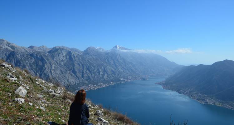 Een persoon die op een heuvel zit met uitzicht op een fjord.