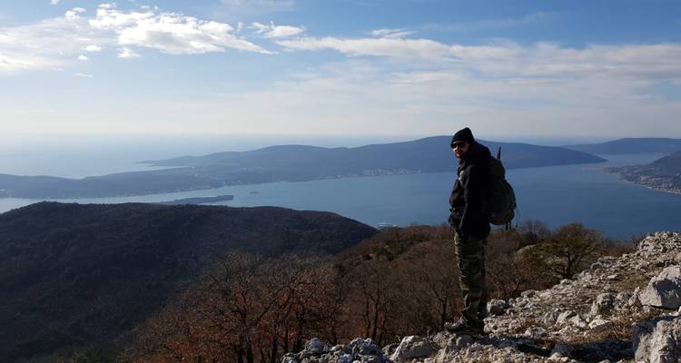 Persoon die op een rotsachtige top staat en uitkijkt over een baai.