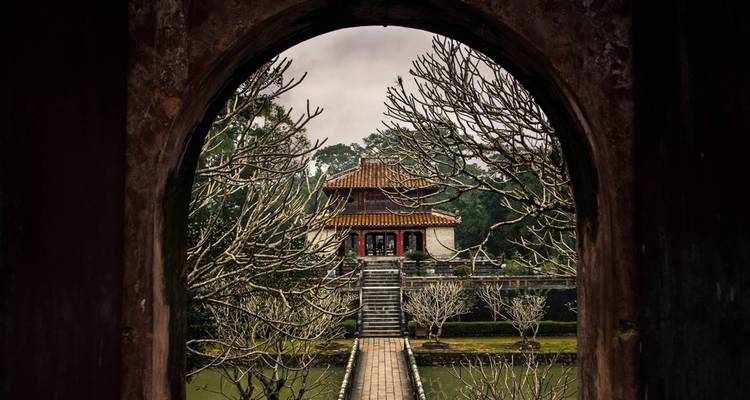 Templo visto a través de una puerta circular con un árbol seco en primer plano.