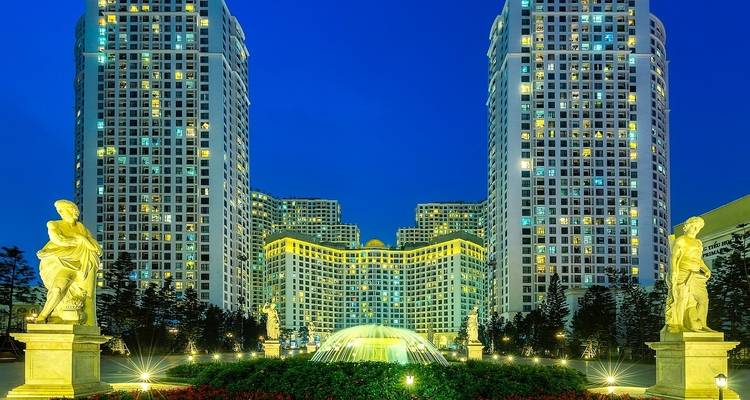 Gran edificio con estatuas doradas y una fuente, iluminado por la noche.