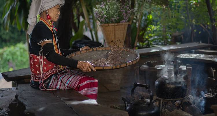 Mujer en vestimenta tradicional cerniendo frijoles sobre el fuego.