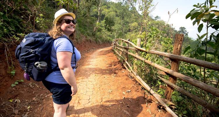 Woman hiking on a dirt path in a lush forest.