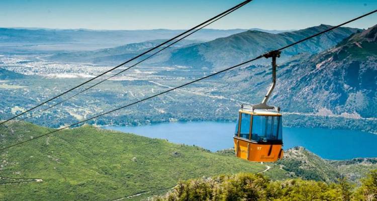 La góndola naranja brillante se desliza sobre un lago azul profundo rodeado de montañas verdes cerca de Bariloche