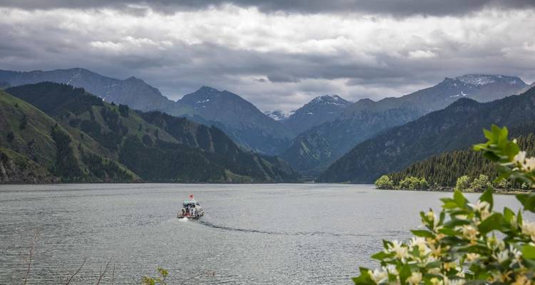 Een boot op een serene meer met een bergachtige achtergrond onder een bewolkte hemel.