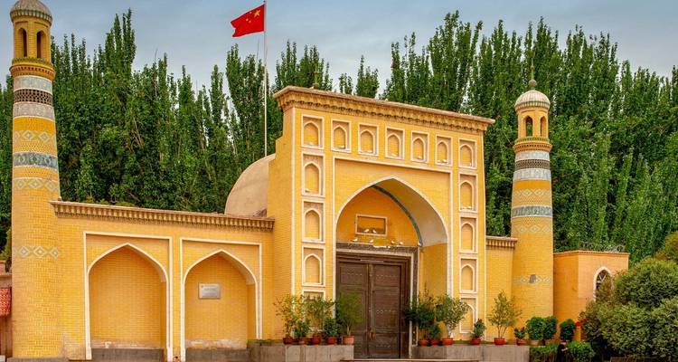 Helder gele moskee met een Chinese vlag voor bladrijke bomen.