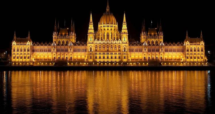 El Edificio del Parlamento Húngaro brillantemente iluminado de noche reflejándose perfectamente en el río Danubio.