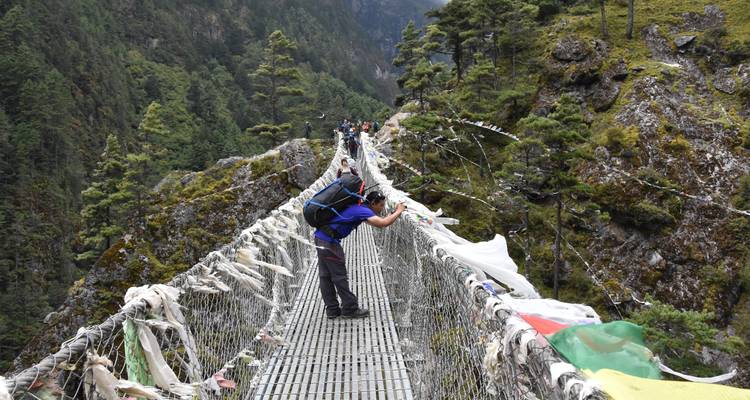 Wandelaars die een hangbrug oversteken met gebedsvlaggen.