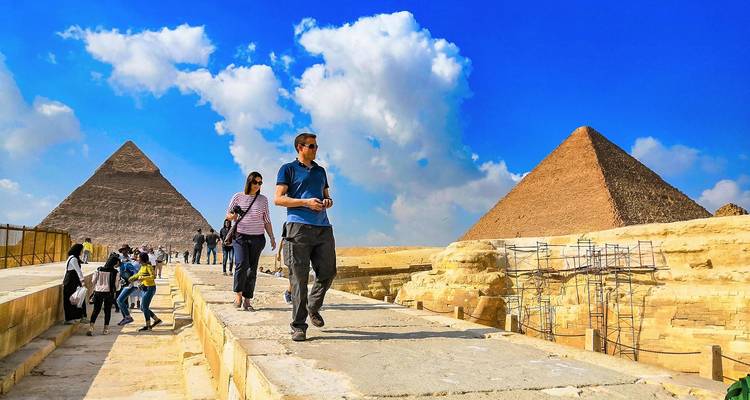 Turistas caminando cerca de las pirámides con un cielo azul claro.